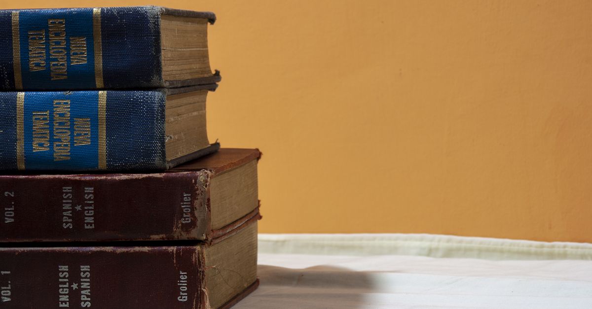 A close-up of vintage English-Spanish dictionaries stacked on a table against a warm backdrop.